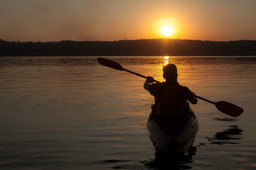 A man paddling on kayak silhouette in sunset, look from the back