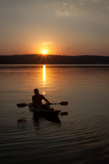Fototapeta na wymiar A man with paddle having a rest in kayak silhouette in sunset