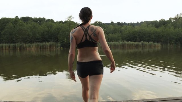 Young brunette girl in a swim suit throws off her shirt and dives into a pond