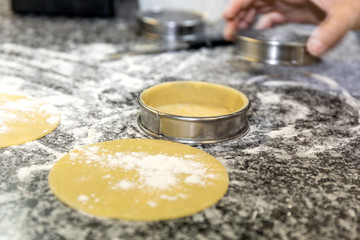 Fototapeta na wymiar Pastries cooked on a bench top of a kitchen. The hand of the pastry chef is holding a round mold. 
