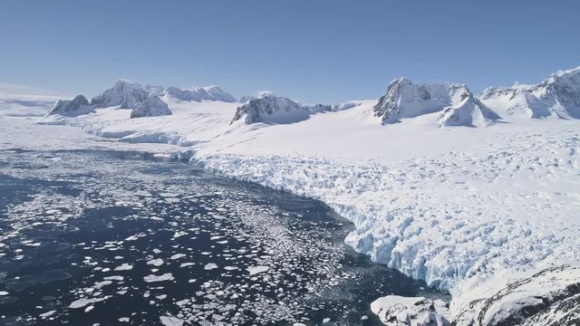 Aerial Flight Over Snow, Ice Frozen Antarctica Shoreline. Winter Landscape. Pieces Of Ice Floating In Polar Ocean. Snow Covered Surface Of Antarctic Coast. Wilderness. 4k Footage.