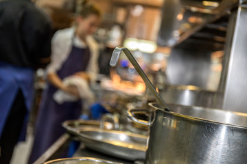 People in the kitchen of a restaurant with a cooking pot in the foreground 