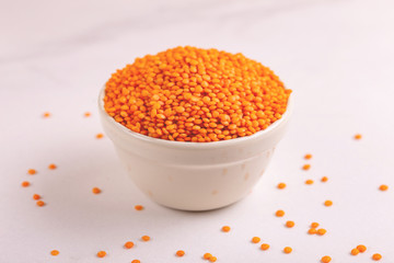 Raw red lentils in clay bowl on white marble background