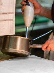 Chef mixing food in a cooking pot. The chef is holding the mixer and the cooking pot. 
