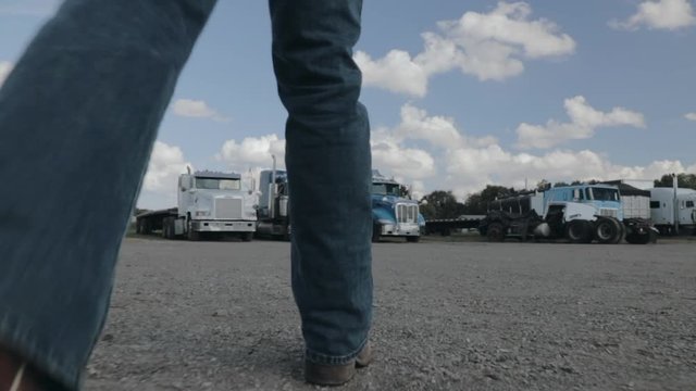 Guy walking on gravel towards parked trucks in cowboy boots ground view