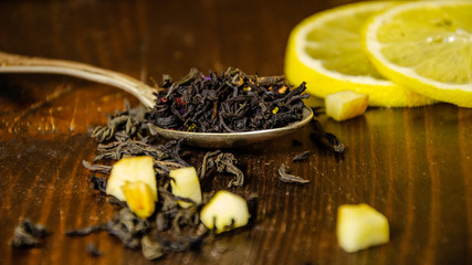 Dry tea leaves in a teaspoon, lemon, wooden table