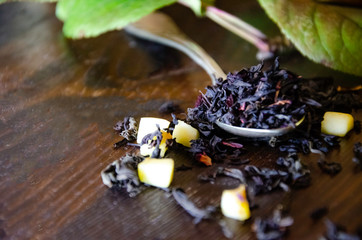 Obraz na płótnie Canvas dry tea leaves in a teaspoon, lemon, wooden table