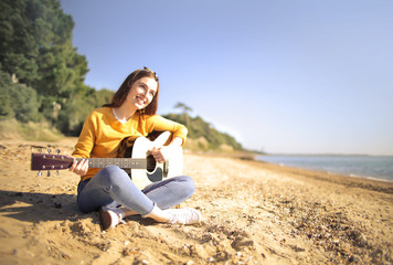 Naklejka na ściany i meble Beautiful girl relaxing at the beach, playing a guitar