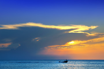 Fototapeta na wymiar Colorful seascape image with shiny sea and speedboat over cloudy sky and sun during sunset in Cozumel, Mexico