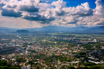 Sunbeam passing through the cloud over Chiangrai city with green grass field and mountain range. the areal shot has been taken through Airplane window.