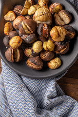 Roasted chestnuts in cast iron grilling pan over rustic wooden board.