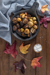 Roasted chestnuts in cast iron grilling pan over rustic wooden board.