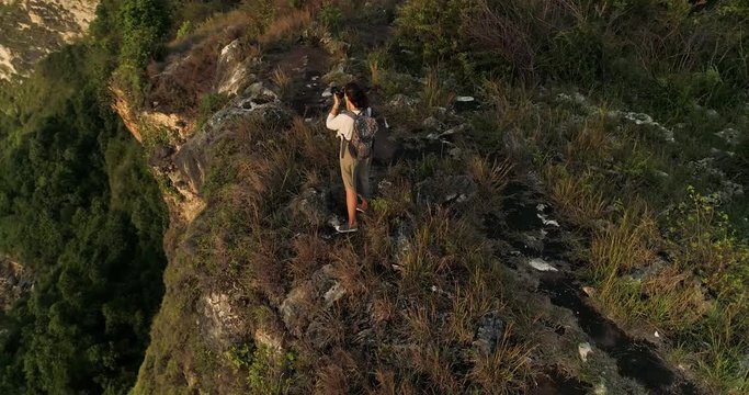 Aerial shot of girl travel photographer on edge of cliff taking photos of seascape 4K