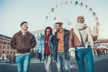 Low angle positive men talking with pleased women while walking together on street during winter