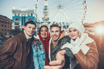 Come with us. Portrait of cheerful men and satisfied girls hugging while standing near each other during winter holiday outdoor