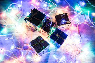 Several boxes of christmas gifts and colorful lights on a wooden background