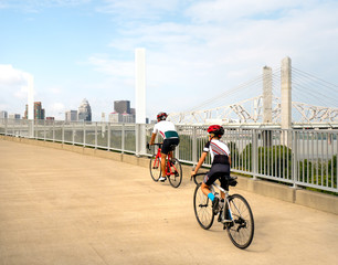 People bike on Louisville bridge urban path with city skyline in background