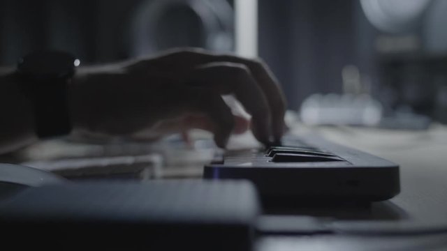 Close up on producer / musician hand playing a melody riff on a MIDI keyboard in the studio with a dimmed light