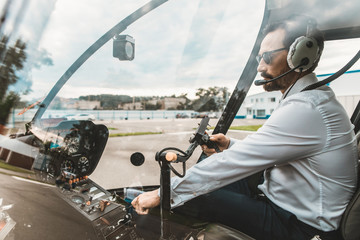 Serious professional pilot sitting in the helicopter cabin and pushing the buttons on the dashboard © Yakobchuk Olena