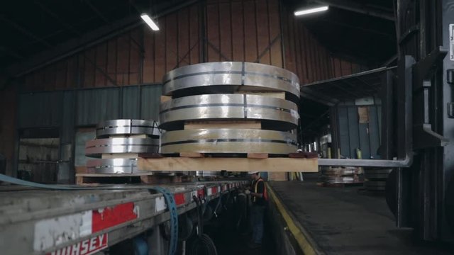 Forklifter unloading heavy steel coils skids from flatbed trailer
