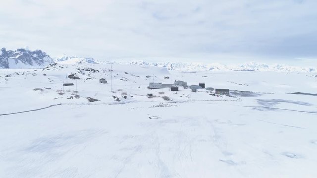 Aerial Zoom Flight Over Antarctica Penguins Colony, Vernadsky Station. Snow Covered Surface, Mounts Of South Pole. Base Among Winter Snow Landscape. Drone Zoom Out Overview. 4k Footage.