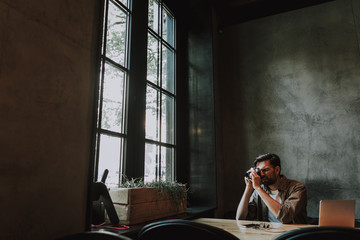 Side view concentrated bearded man taking photo on camera while sitting at table in cozy cafe