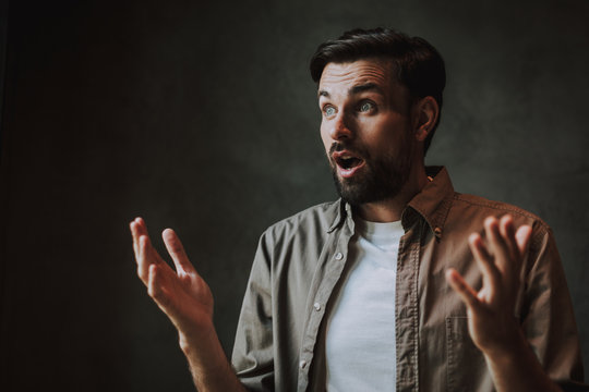 Portrait of surprised man with open mouth flourishing arms while grimacing face