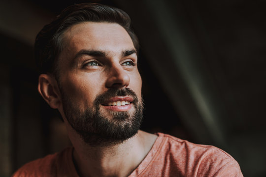 Portrait of happy bearded man with attractive smile dreaming. He situating indoor during rest