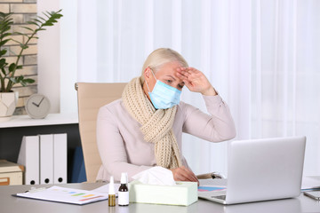 Ill mature woman with face mask suffering from cough at workplace