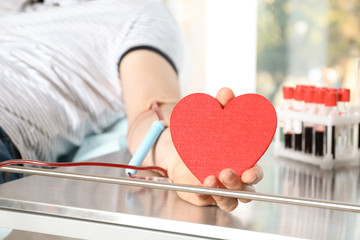 Man holding heart while making blood donation at hospital, closeup