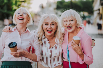 Waist up portrait of three laughing grannies walking around the city while holding coffee and...