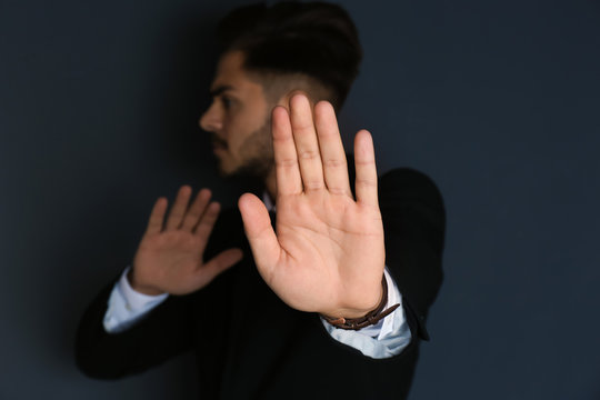 Man showing stop gesture on dark background. Problem of sexual harassment at work