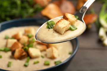 Spoon with fresh homemade mushroom soup over bowl, closeup