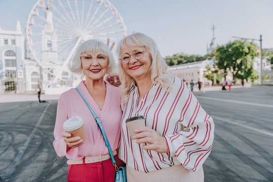Waist up portrait of smiling adult women holding coffee with ferris wheel on background