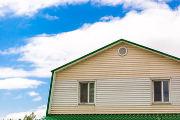 roof of the attic with two windows in the house against the blue sky with clouds