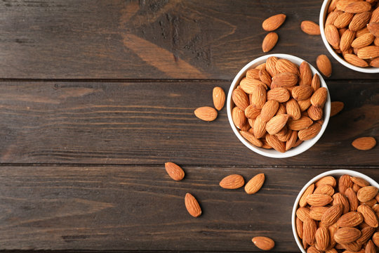 Tasty organic almond nuts in bowls and space for text on table, top view