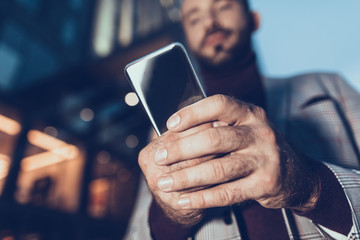 Calm man standing alone and looking at the screen of his gadget while holding it