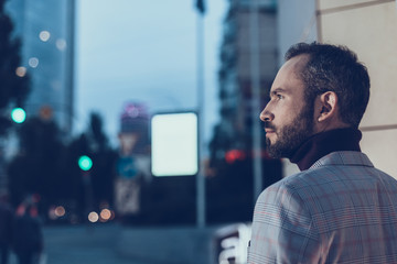 Calm young man thoughtfully looking into the distance while being outdoors alone