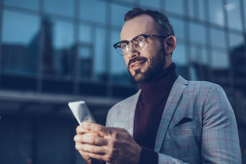 Attractive smiling man feeling interested and looking into the distance while standing with his modern device