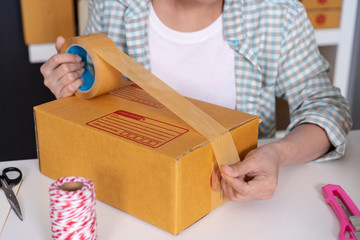 Fototapeta na wymiar hand of woman online entrepreneur using tape to packing parcel box at home office, prepare product for deliver to customer.