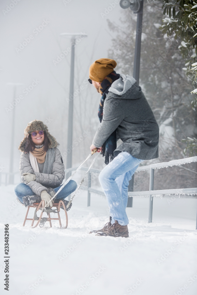 Wall mural Young couple with sled playing in snow in nature