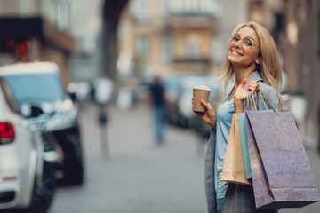 Waist up portrait of charming middle-aged lady holding cup of coffee and shopping bags. She is...