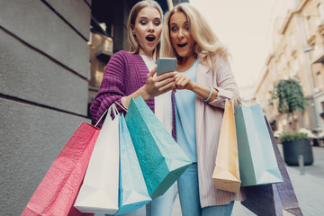 Just look at this. Low angle portrait of elegant girl with shopping bags holding cellphone while...