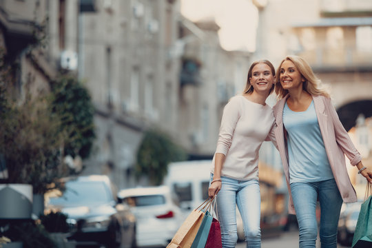 Portrait of beautiful young lady spending time with mother outdoors. They hugging and smiling while carrying shopping bags