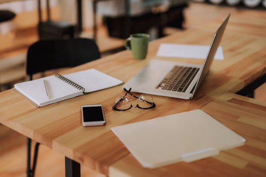 Wooden desk with white notebook, smartphone, cup of coffee, eyeglasses and documents