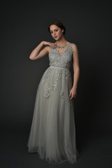 full length portrait of brunette  girl wearing long silver ball gown. standing pose on grey studio background.