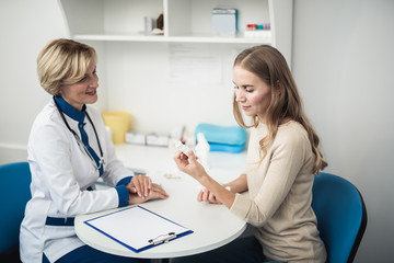 Concept of professional consultation and remedy. Waist up side on portrait of lady doctor and young female patient with running nose holding nasal drops