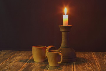 Romantic evening together. Ceramic coffee cups and an old rare ceramic candlestick of an unusual shape with a burning candle on a dark wooden background.