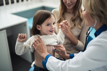 Concept of professional consultation in therapist practice. Close up portrait of pediatrician woman examining girl by stethoscope in medical office