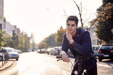 street (out of focus in background), one young man posing in foreground, looking sideways,  bicycle handlebar outdoors. 20-29 years old, wearing suit.